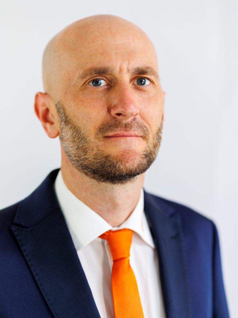Patrick Kastler FingerHaus Porträt eines Mannes mit kurzem, glattem Haar und einem leichten Bart, in einem weißen Hemd.